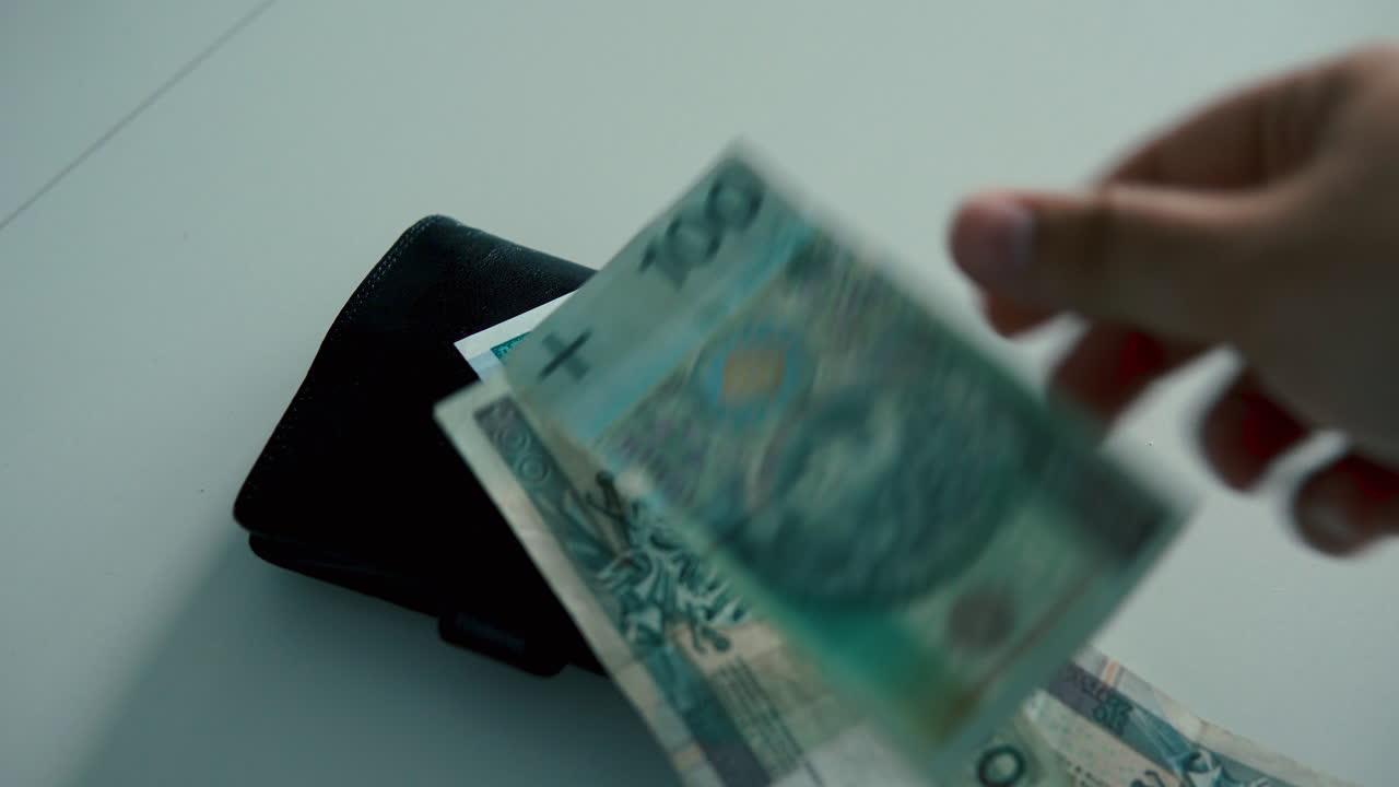 테이블에 있는 검정 가죽 지갑 위에 폴란드 지폐를 세고 놓은 사람