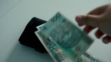 persona contando y colocando billetes polacos encima de una billetera de cuero negro en la mesa