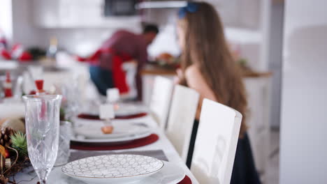 Hija-Ayudando-A-Poner-La-Mesa-Mientras-La-Familia-Se-Prepara-Para-La-Comida-Navideña-En-Casa