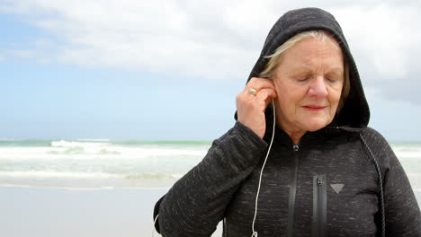 Vorderansicht-Einer-Alten-Kaukasischen-Seniorin,-Die-Am-Strand-4k-Musik-über-Kopfhörer-Hört