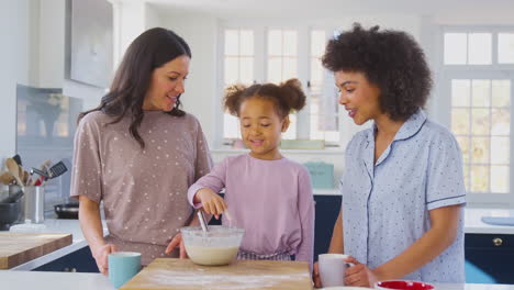 Familie-Mit-Zwei-Müttern-Im-Schlafanzug,-Die-Zu-Hause-Mit-Ihrer-Tochter-Morgenpfannkuchen-In-Der-Küche-Backen