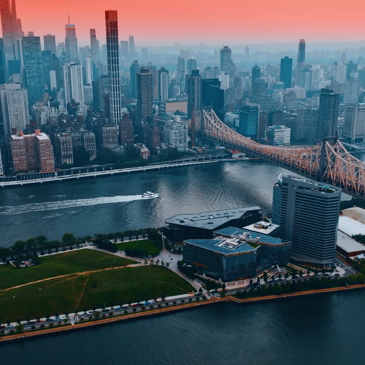 Queensboro Bridge or 59th Street Bridge over East River. Motor boat floating by the water. New York skyline under pink sky at backdrop