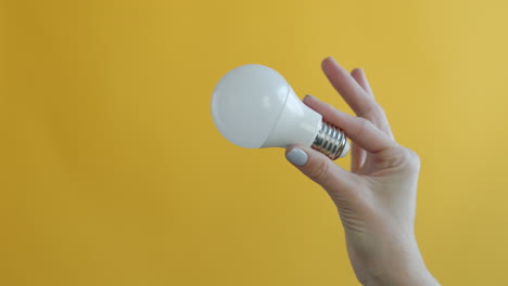 hand holding an led light bulb against a yellow background