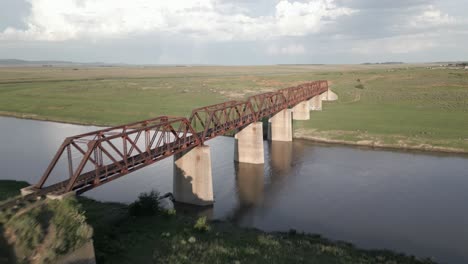 Low-aerial-flight-to-rusted-steel,-abandoned-railway-bridge-over-river