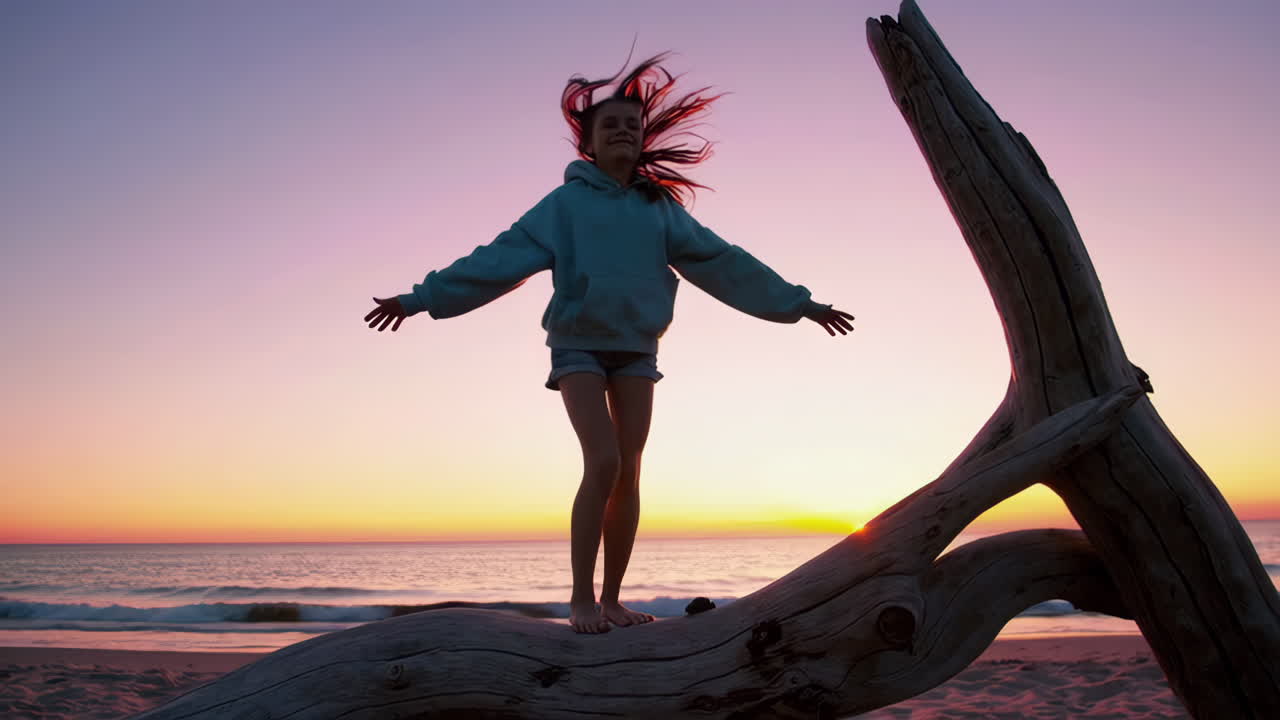 Girl standing on driftwood at sunset