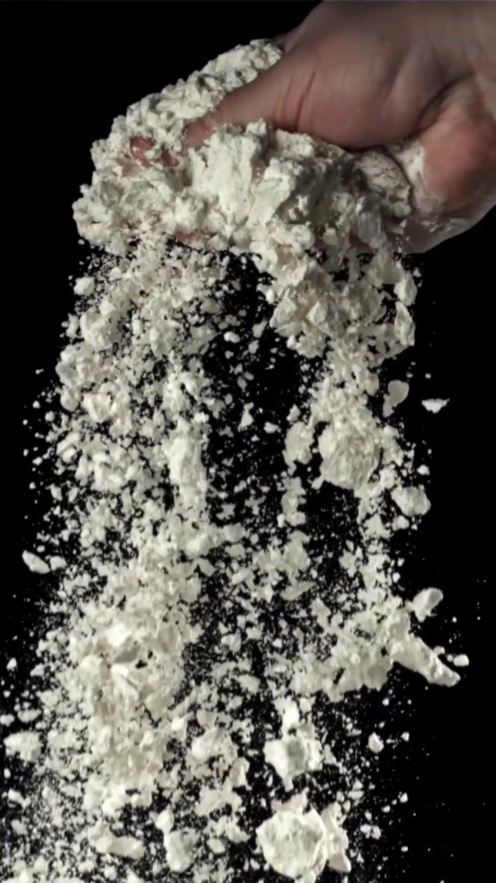 Hand som häller vitt mjöl i slow motion mot svart bakgrund