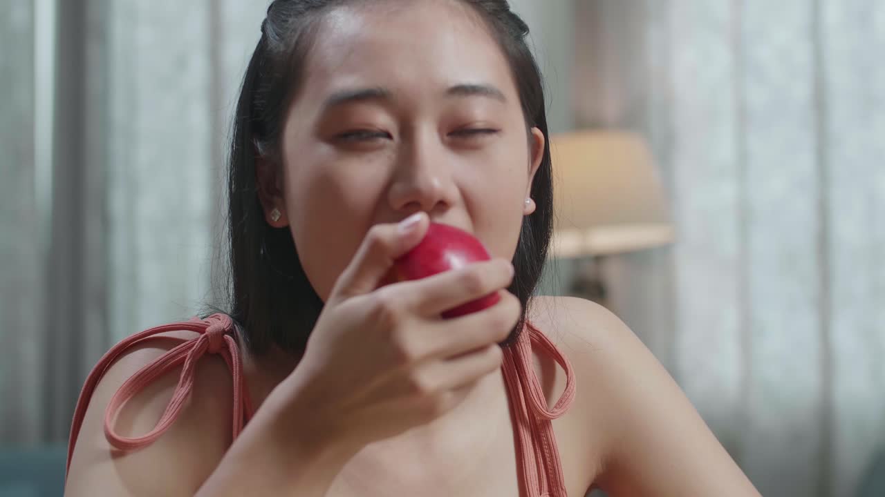 un primer plano de una mujer asiática feliz mordiendo una manzana mientras come comida saludable en casa