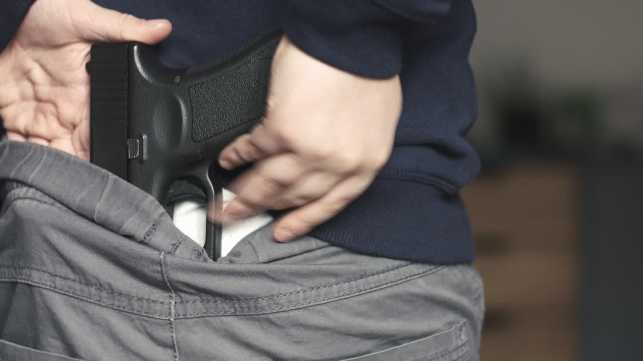 primer plano de un niño colocando una réplica perfecta de una pistola de juguete de nueve milímetros en la parte trasera de sus pantalones y luego escondiéndola debajo de su sudadera