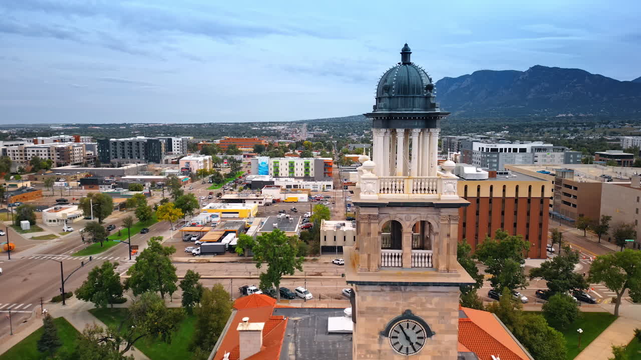 Flying up to the clock tower of Colorado Springs Pioneers Museum. Lively downtown of Colorado Springs, Colorado, USA from drone. Huge mountain at backdrop