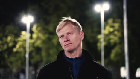 retrato de hombre rubio deportivo estirando el cuello antes de entrenar en el parque por la noche