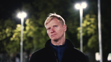 portrait of sportive blond man stretching neck before training in the park at night