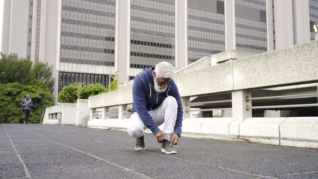 Senior African American man jogging urban track, stopping, tying shoe lace and checking wristwatch