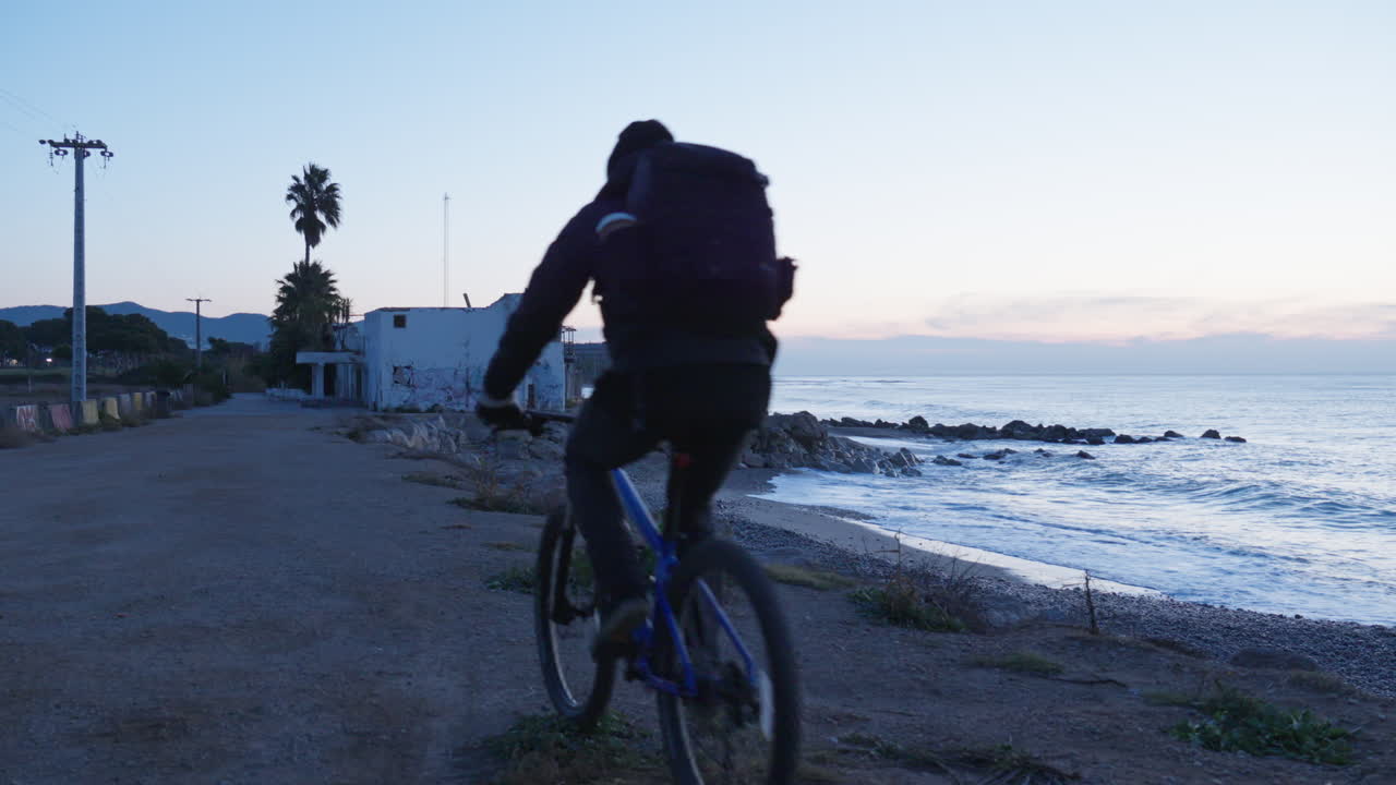 한 여행자가 비치 하우스를 향해 자전거를 타고 푸른 시간 동안 바다의 전망을 감상하기 위해 바위가 많은 해안 가장자리에 멈춥니다.