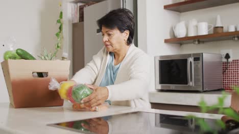 mujer biracial senior agarrando verduras de la caja en la cocina sola