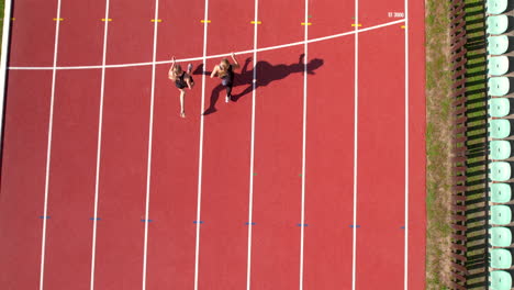 aerial shot of two athletes running in sync along a curved section of a red track, shadows extending to the side, captured from above