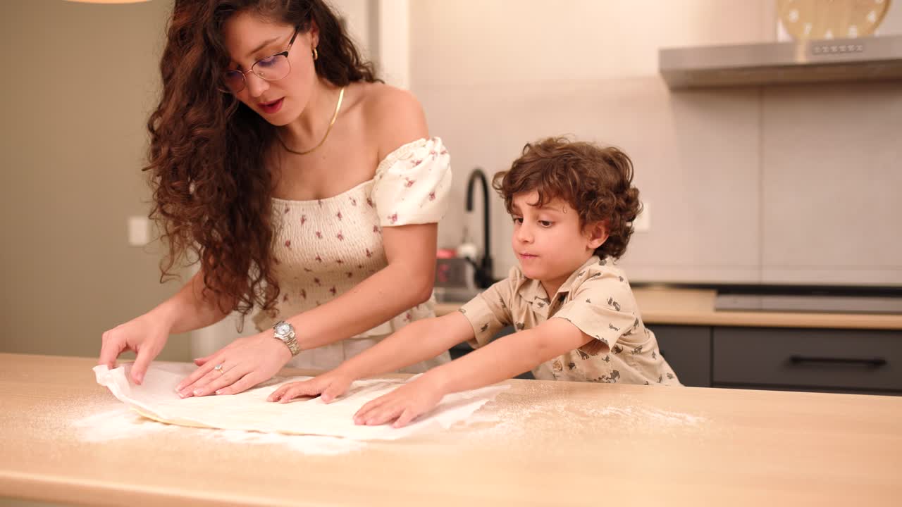 Mother and son removing rolled dough from paper in kitchen