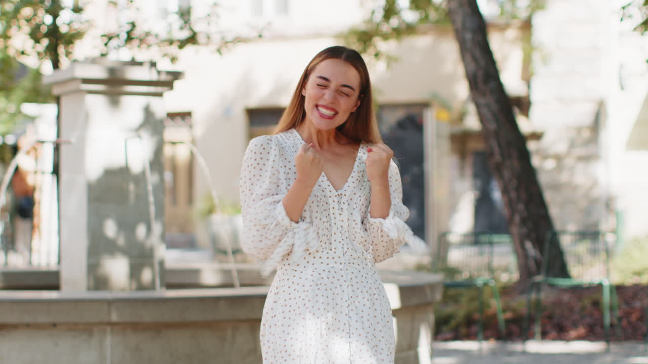 흥분한 젊은 여성이 소리를 지르며 성공을 축하하고 승리하는 성취를 축하하고 도시 거리에서 좋은 소식을 전합니다.