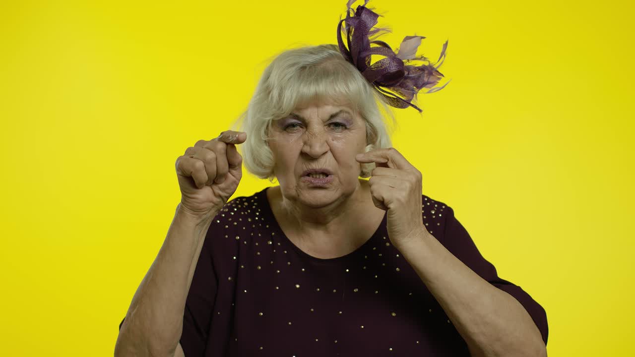 Anziana signora scontenta e infastidita che fa un gesto sciocco. Nonna anziana su sfondo giallo