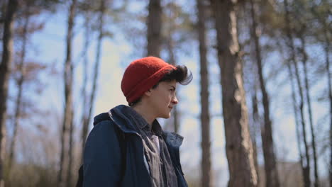 een jonge vrouw met kort haar in een rode wollen muts kijkt rond in het bos 1