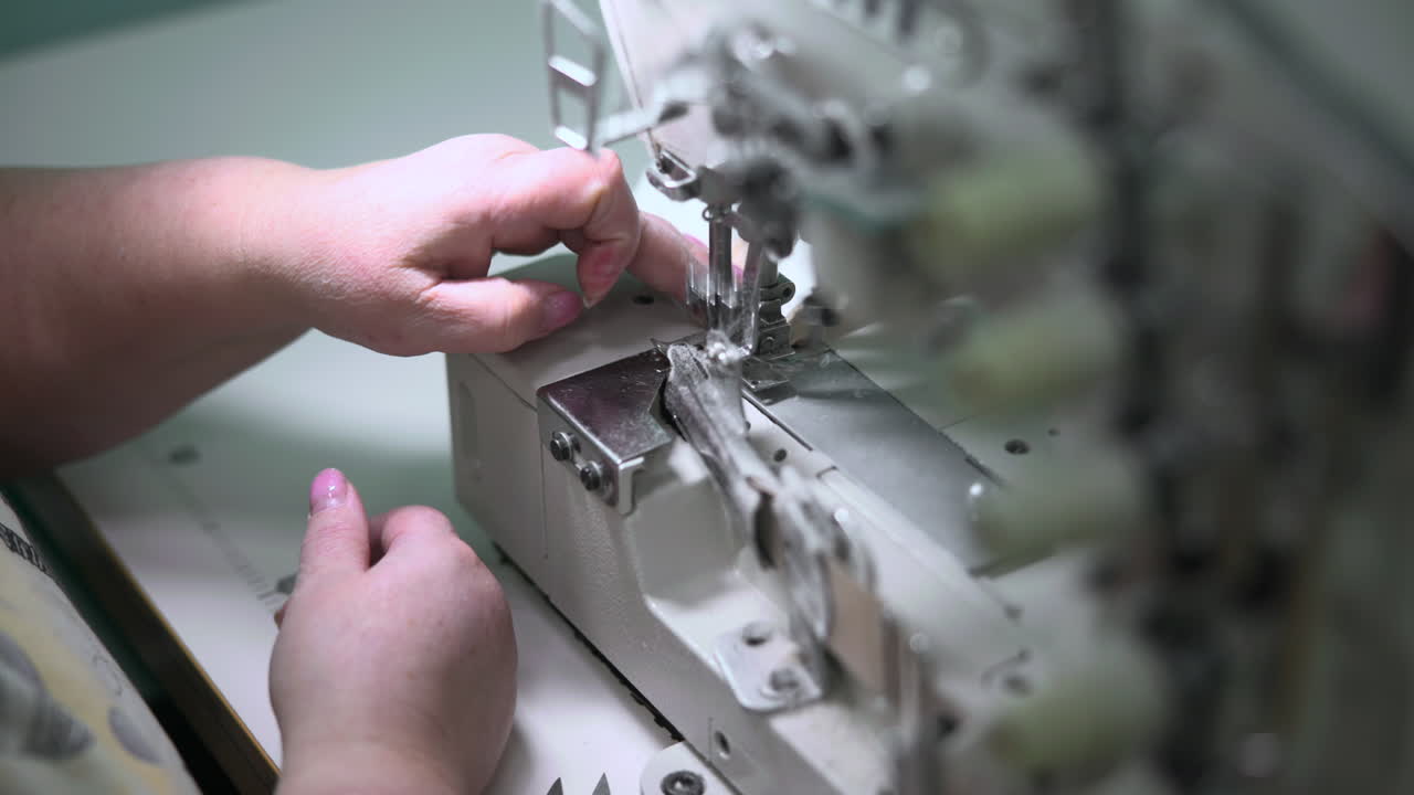 White Factory Sewer Operating Overlock Machine On Seam, Closeup Hands Guiding Edge Through Fast Serger. Media