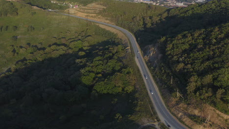 Cars-moving-on-a-mountain-road-and-a-city-in-background,-on-the-sunset,-Russia,-Far-East