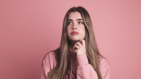 pensive young woman standing with finger at mouth