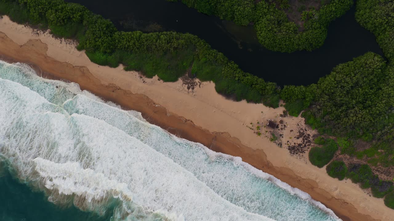 Slow motion aerial shot of strong ocean waves crashing on golden beach with dense green mangroves and dark lagoon. Punta Perula, Mexic