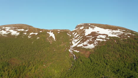 vista aérea con vistas a una cascada en una montaña nevada, soleado, día de verano, en rotsund, troms, nordland, noruega - seguimiento, disparo de drones