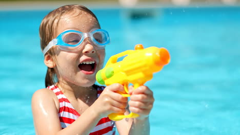 young girl playing with a water gun in a swimming pool