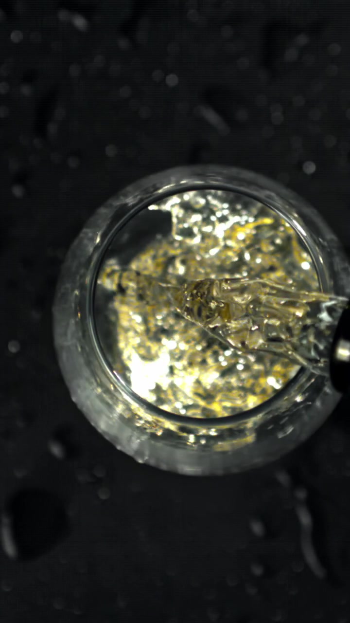 Versamento al rallentatore di liquido trasparente in un bicchiere con riflessi dorati