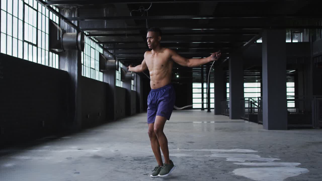 Shirtless african american man skipping the rope in an empty urban building