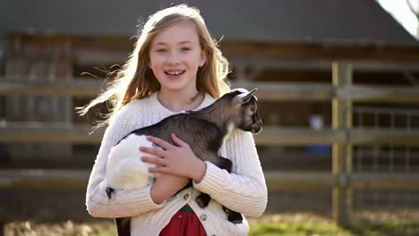 happy girl holding adorable baby goat on a farm