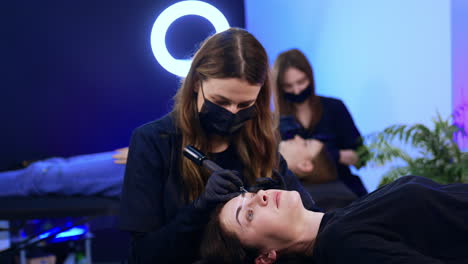 brunette woman lies on the couch having her eyebrows tattooed. salon procedure of permanent make up.
