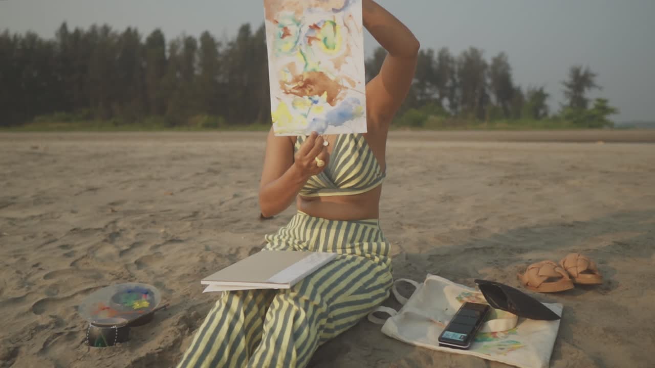 жизнерадостный художник, вдохновленный солнечным пляжем, показывает художественное произведение уже после того, как оно написано и задумано