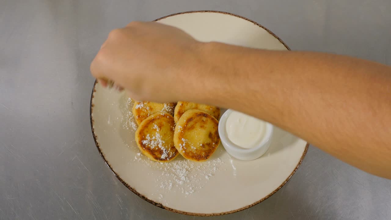 요리사는 접시에 설탕 가루로 치즈 팬케이크를 장식합니다.