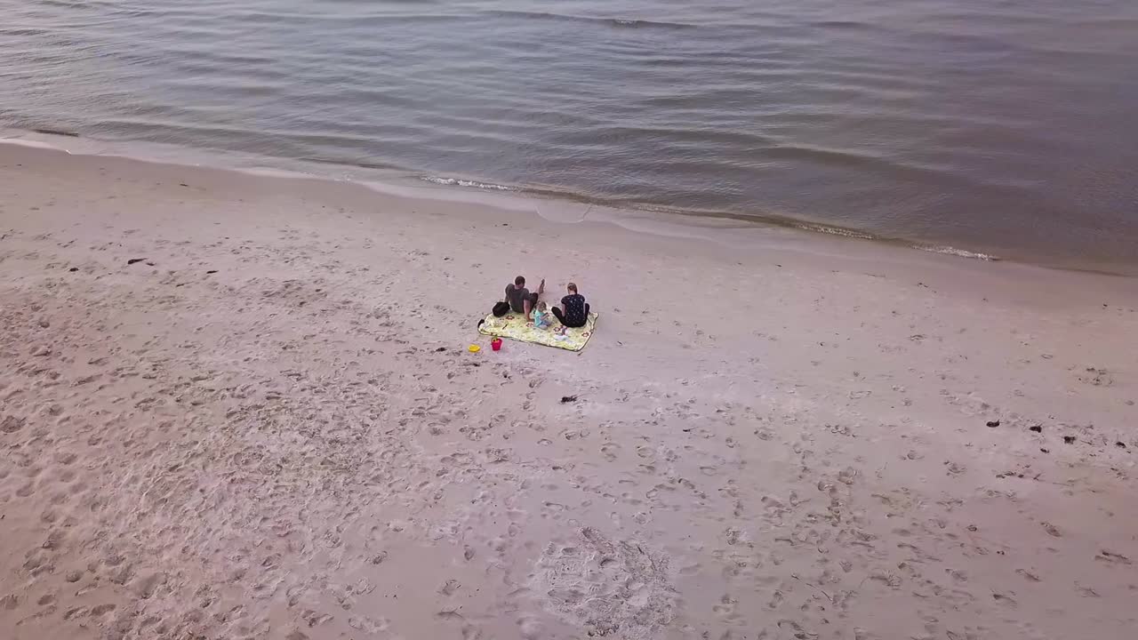 Aerial Shot of a Family Ralaxing on a Sandy Beach on a Cloudy Day. Happy Family on Beach. Family Vacation.