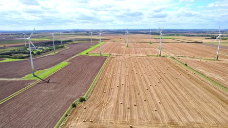 Oben-Zeigt-Ein-Luftvideo-Eine-Malerische-Szene:-Windkraftanlagen-Drehen-Sich-Anmutig-Auf-Dem-Kürzlich-Abgeernteten-Feld-Eines-Bauern-Aus-Lincolnshire,-Im-Blick-Sind-Goldene-Heuballen