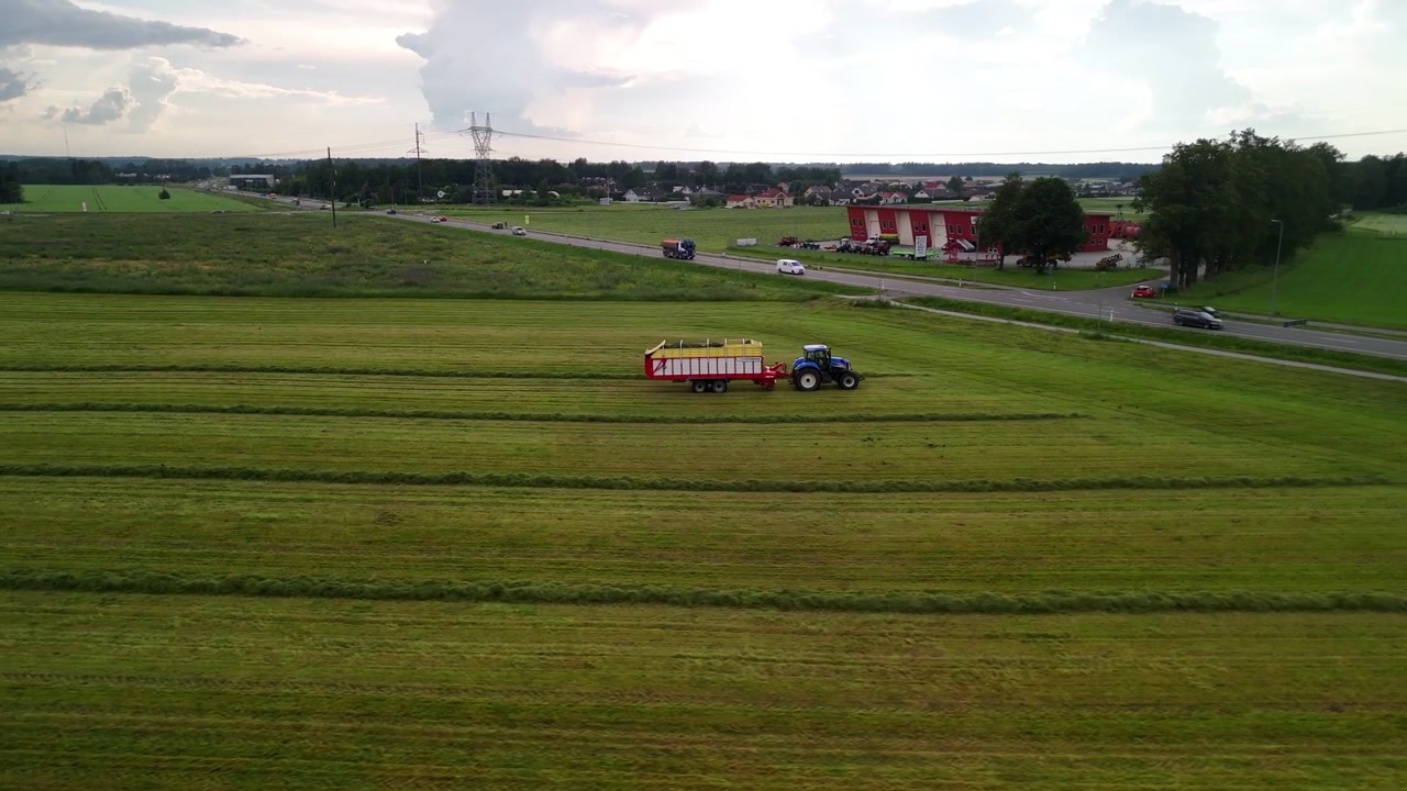 Vecchio trattore che raccoglie file di fieno create da un voltafieno | Riprese con drone.