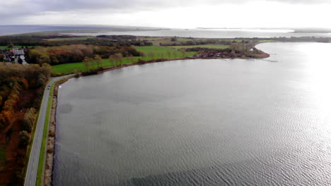 cars driving on road between schlei sea and forest in autumn, tilt up aerial
