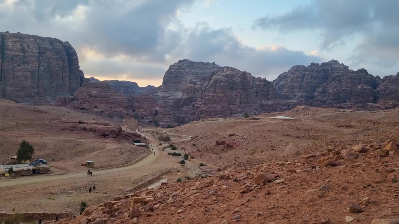 Vista panorámica del escarpado paisaje desértico de Petra, Jordania, con imponentes acantilados de arenisca, valles profundos y espectaculares formaciones rocosas bajo un cielo nublado al atardecer, belleza natural.