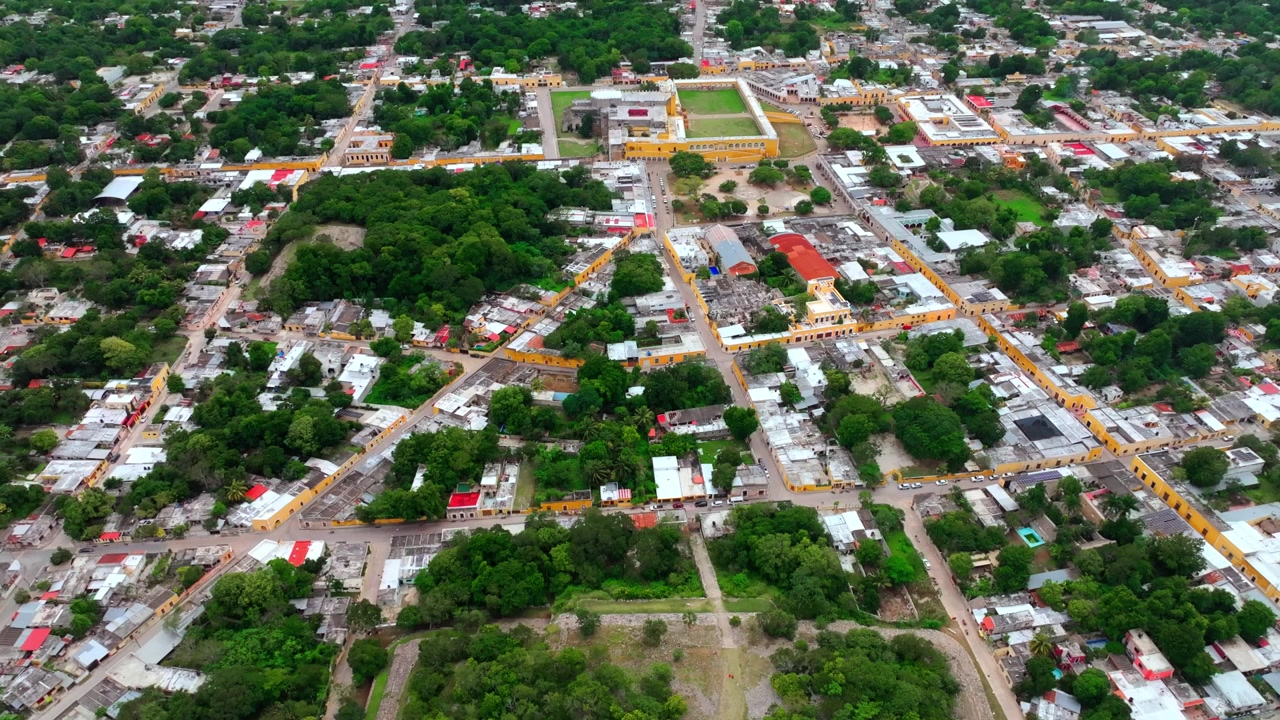 Vista aérea sobre as ruas e casas de Izamal, Yucatán, México, com o traçado urbano colonial estendendo-se entre manchas de vegetação tropical.
