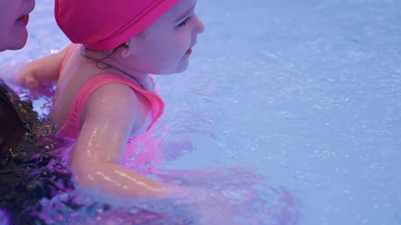 Close view of toddler dabbing tiny hands on pool water surface, enjoying ripples and splashes with playful expression, showing innocence and curiosity during aquatic leisure in warm daylight