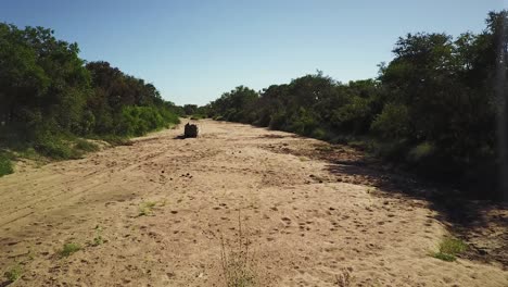 drone shot tracking a game vehicles in a dried up riverbed in the heat of the african afternoon sun