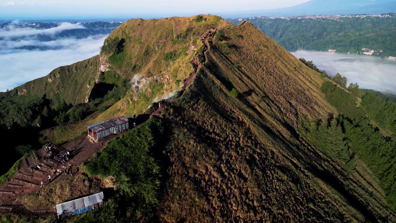 Sentiero di montagna con escursionisti sopra un mare di nuvole, fumo vulcanico che si innalza attraverso un suggestivo paesaggio tropicale con terreno ripido ad alta quota, riprese aeree con drone.