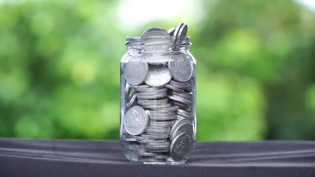 Coins of money falling down on the glass full of coins with blur nature background