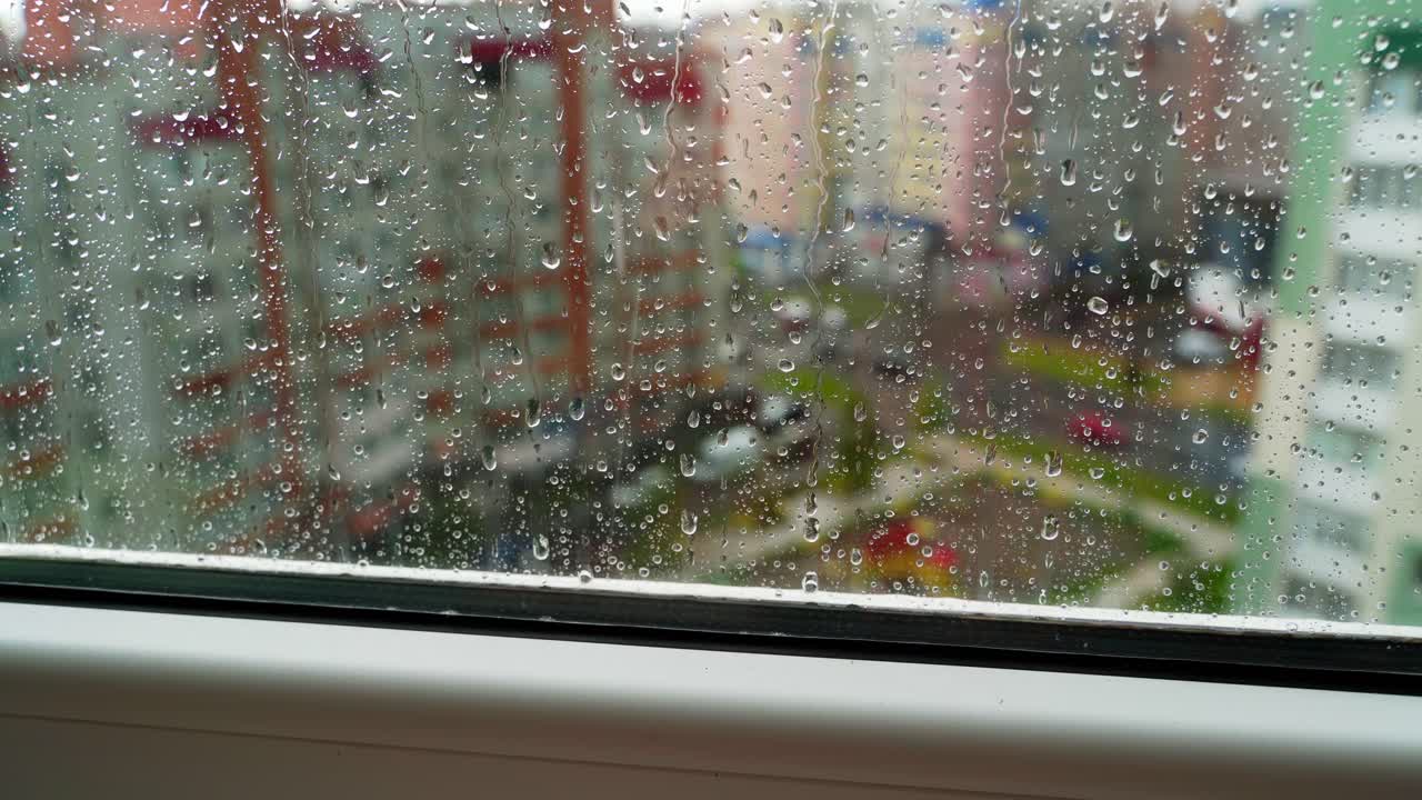 Glass window in rainy weather. Raindrops falling down on the urban background. View from the flat on the rainy weather in the city.
