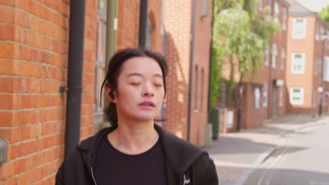 young woman exercising running along urban street wearing wireless earbuds