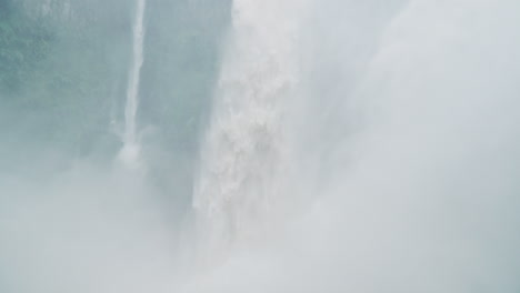 man takes in bajos del toro waterfall and spray blowing off, slow motion