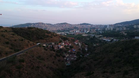 arial drone shot of the hills and mountains behind barcelona, towards a small village on the side of cliff as a car drives down the hill