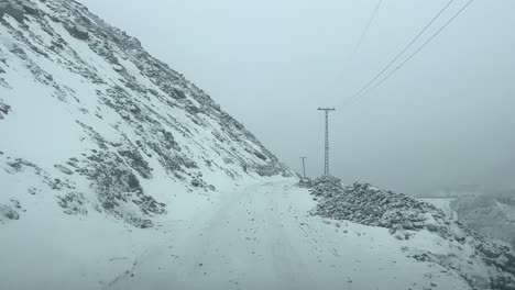 POV-Driving-Along-Snow-Covered-Road-On-Mountainside-Through-Skardu-City,-Gilgit-Baltistan-With-Low-Visibility